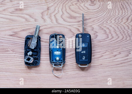 Broken or damaged remote key fob and new vehicle key on wooden background. Broken or damaged remote key fob of any vehicle car service.- Image Stock Photo