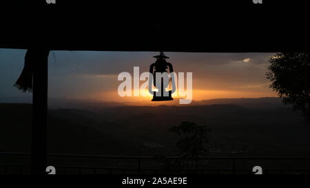 Paraffin oil lantern hanging from a beam silhouetted against a setting sun Stock Photo
