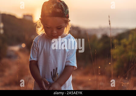 Cute little boy on the walk, sweet child with pleasure spending time outdoors, enjoying warm summer evening and beautiful sunset Stock Photo