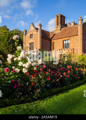 Portrait of Chenies Manor House from garden.Fine weather, blue sky and ancient brickwork in the sun with September blooming dahlias, cosmos and roses. Stock Photo