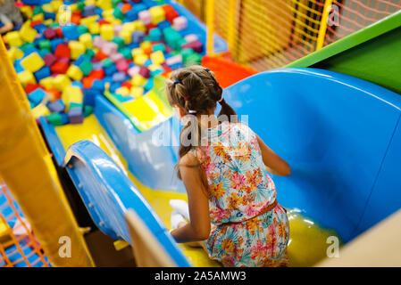 Little girl riding on plastic kids slide, playroom Stock Photo