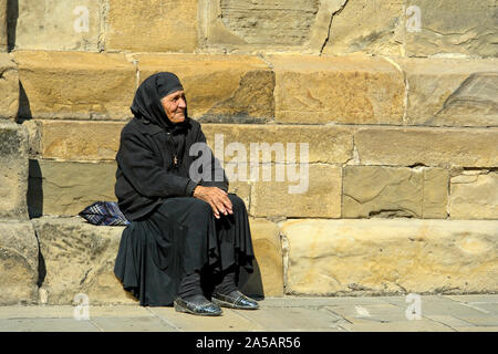 Old Georgian woman in black dress sitting on a stone at the Svetitskhoveli Cathedral, Mtskheta, Georgia Stock Photo