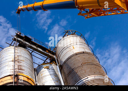 Crane is carry and keeps balance with heavy metal silo in industrial complex. Stock Photo