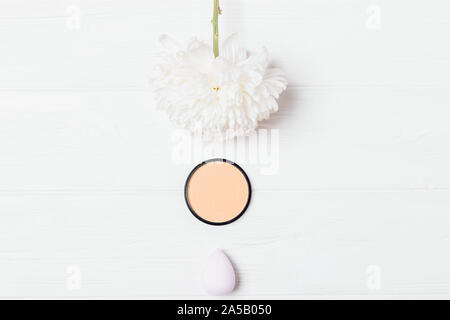 Makeup face powder and sponge blender next to fresh delicate chrysanthemum flower on white background, minimal flat lay composition. Stock Photo