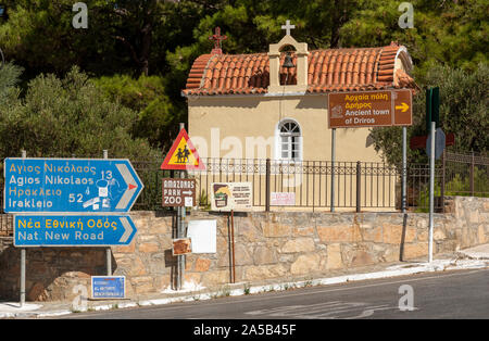 Neopolis, northern Crete, Greece.2019.  On the Old National Road as driving into Neopolis a Cretan historic town is a small chapel with blue road sign Stock Photo