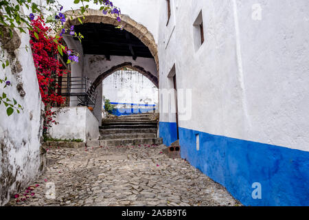 Close-up detail view of cobblestone alleys between whitewashed and colourful building walls in landmark town of Obidos, Portugal Stock Photo