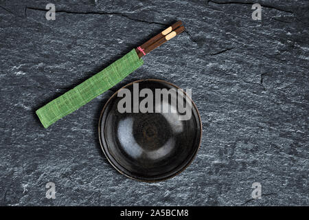Empty bowl and chopsticks over background texture black shist with oblique light Stock Photo