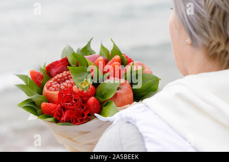 Woman holds in her hands a beautiful bouquet of apples, pomegranate, strawberries and flowers Stock Photo