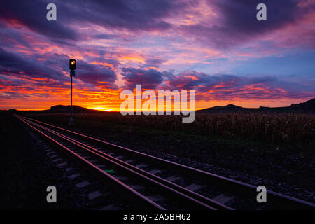 Morning train to the hell. Old Railway tracks running through a field stretch to rural countryside at dramatic sunrise. Stock Photo