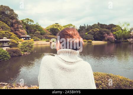 Female enjoying the view of a pond and trees with a cloudy sky in the background shot from behind Stock Photo