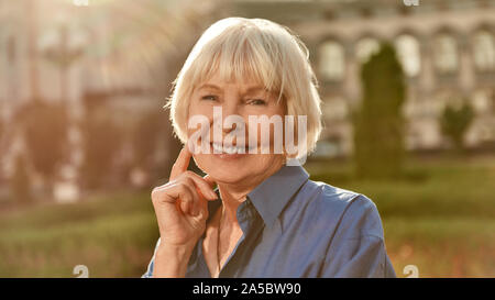 Portrait of happy and beautiful senior woman looking at camera and smiling while standing outdoors on a sunny day Stock Photo
