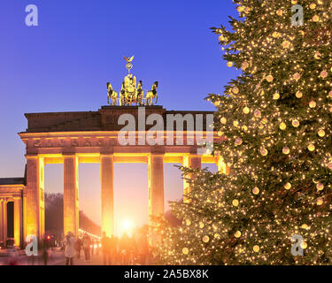 Brandenburg Gate in Berlin with golden Christmas tree in evening illumination on a sunset with Sun setting through the gate. Stock Photo