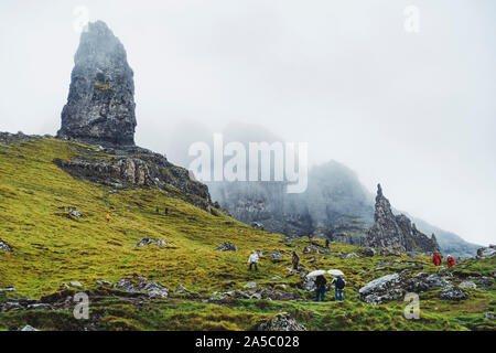 Tourists don raincoats and umbrellas on a rainy, cloudy day at the Old Man of Storr, a famous rock formation on the Isle of Skye, Scotland Stock Photo