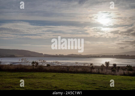 View over an laggon like inlet with the sun about to set behin the mountain range. The reed is swinging in the wind. Stock Photo