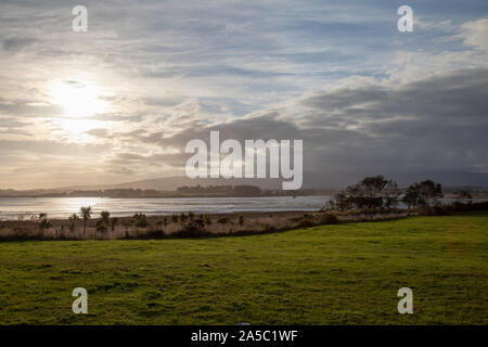 View over an laggon like inlet with the sun about to set behin the mountain range. The reed is swinging in the wind. Stock Photo