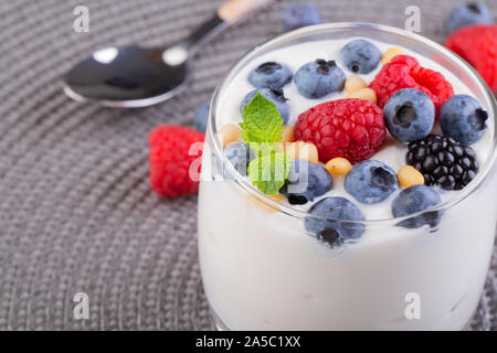 A glass of granola in yogurt with a mix of wild berries on a gray table. Top view, macro shot Stock Photo