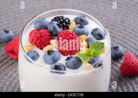 A glass of granola in yogurt with a mix of wild berries on a gray table. Top view, macro shot Stock Photo