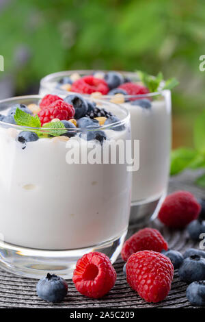 A glass of granola in yogurt with a mix of wild berries on a gray table. Top view, macro shot Stock Photo