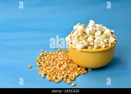 popcorn inside bowl with pink bottom with corn beside on blue background Stock Photo