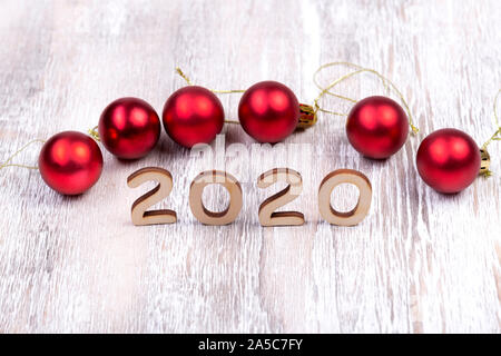 On a light wooden background the numbers 2020, the symbol of the new year and red balls Stock Photo