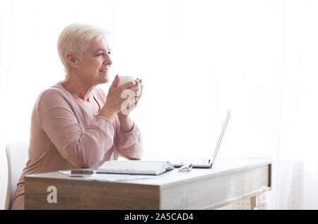Peaceful old lady having coffee break during working day Stock Photo