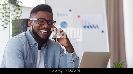 Laughing millennial employee talking on cellphone at workplace in office Stock Photo