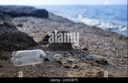 Single use plastic bottle discarded on beach next to sea Stock Photo