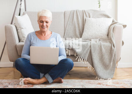 Resourceful mature woman sitting on floor and using laptop Stock Photo