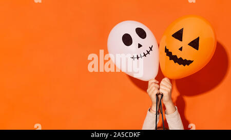 Woman holding two balloons with holiday faces on orange Stock Photo