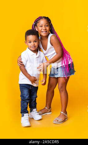 Little black sister hugging her toddler brother on yellow background