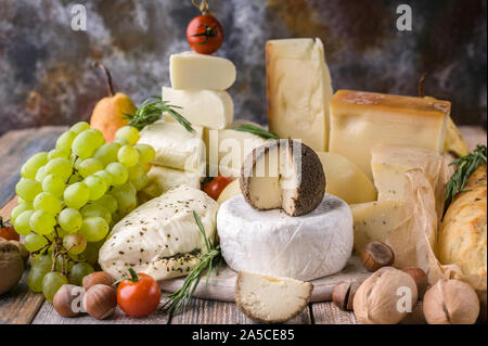 A variety of cheeses, nuts, fruits, spicy herbs and onion baguette on a rustic background. Stock Photo