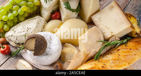 Food banner: Close-up different types of delicious cheeses, nuts, fruits, spicy herbs and onion baguette on a rustic background. Stock Photo