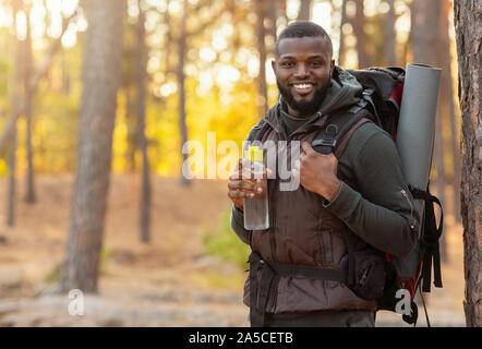 African man wearing backpack standing over forest background Stock Photo
