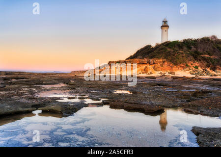 White stone Norah lighthouse on Norah head of Pacific coast in Australia. Scenic sunrise sky and light with reflection of lighthouse in still puddle a Stock Photo