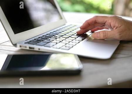 Typing on the keyboard of laptop with cell phone by the side. Outdoor. Flexi work concept. Stock Photo