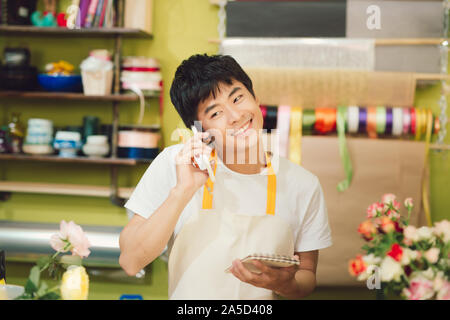 Young florist talking by phone while working with notebook in shop Stock Photo