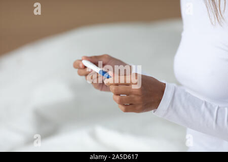 Young mixed race woman holding quick plastic pregnancy test in hands. Stock Photo