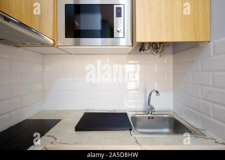 Tiny modern kitchen counter with microwave oven, sink and stove top Stock Photo