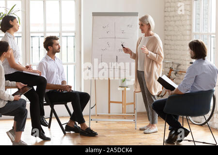 Skilled old female mentor give presentation training staff at meeting Stock Photo