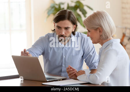 Professional male mentor teaching mature employee explaining computer software Stock Photo