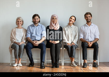 Smiling multicultural professional business people sit on chairs in row Stock Photo