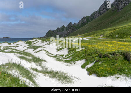 landscape with road between white sand dunes, green meadows and steep rocks at bay on western side of island, shot under bright summer light at Bleik, Stock Photo