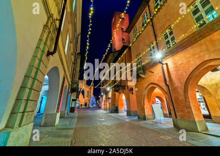 Narrow cobblestone street illuminated with Christmas lights in town of Alba in Piedmont, Northern Italy. Stock Photo