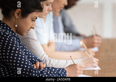 Multinational students seated at desk in row holding pencils writing on papers Stock Photo