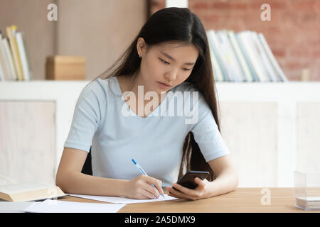 Asian ethnicity schoolgirl do homework seated in library desk Stock Photo