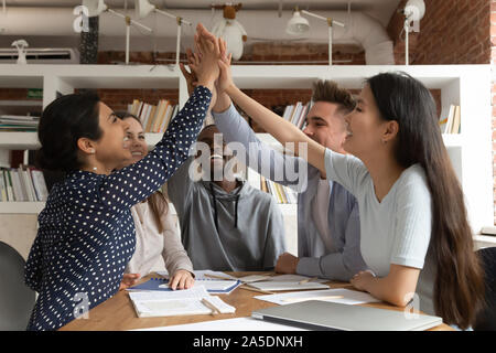 Group of multiracial friends students sit at desk celebrating graduation Stock Photo