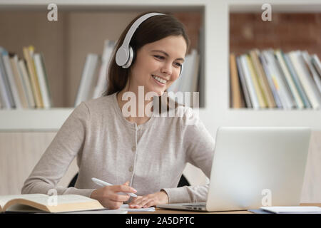 Girl in headphones look at pc screen noting studying indoors Stock Photo