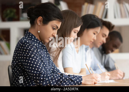 Multiracial students sitting at desk writing on papers doing task Stock Photo