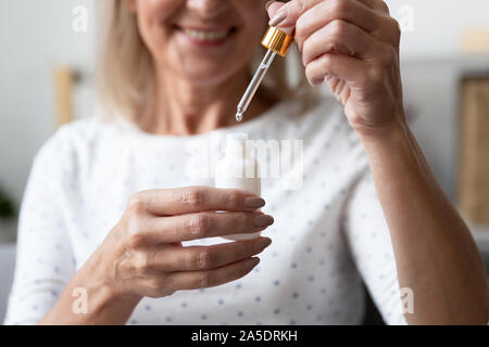 Happy mature woman holding face skin care serum, close up Stock Photo