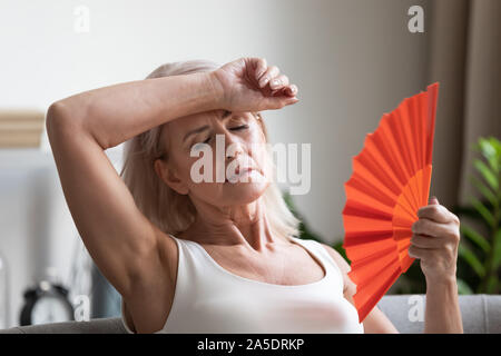 Tired overheated middle aged lady wave fan complain on heat Stock Photo